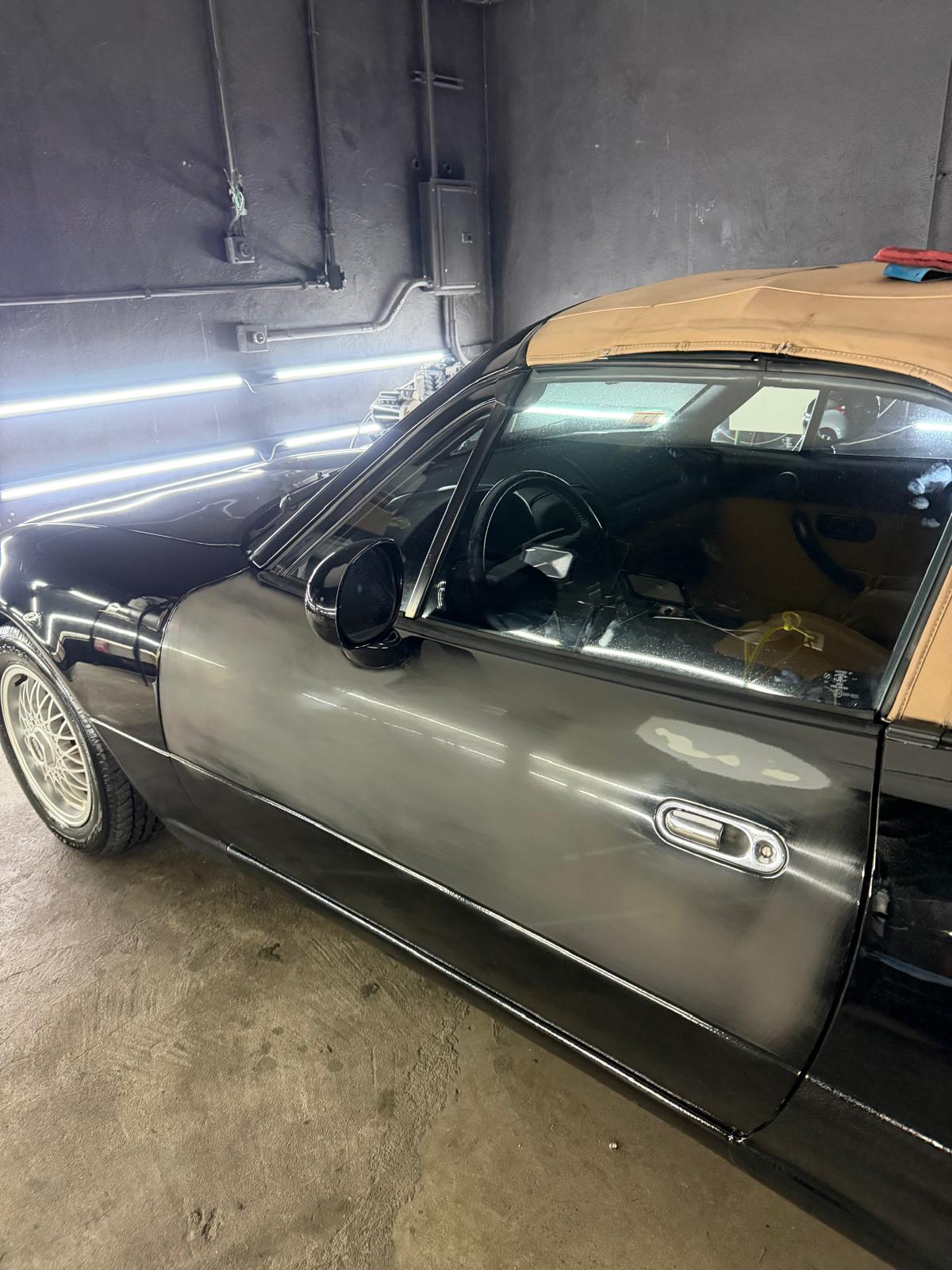Black Mazda Miata door with dull, oxidized paint before correction